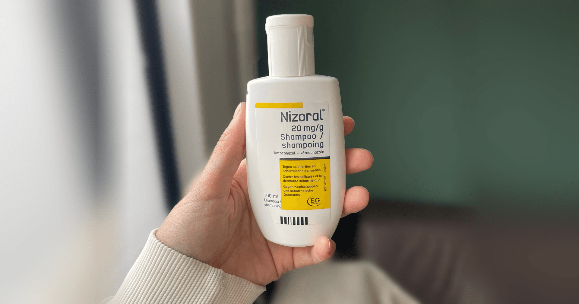 Hand houdt een fles Nizoral 20 mg/g shampoo met ketoconazol vast