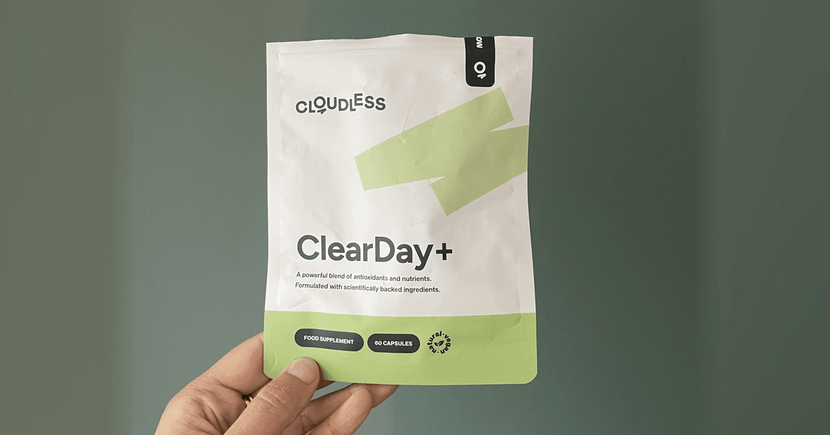 Hand houdt een zakje Cloudless ClearDay+, de oude verpakking van Clear+, voor een groene muur